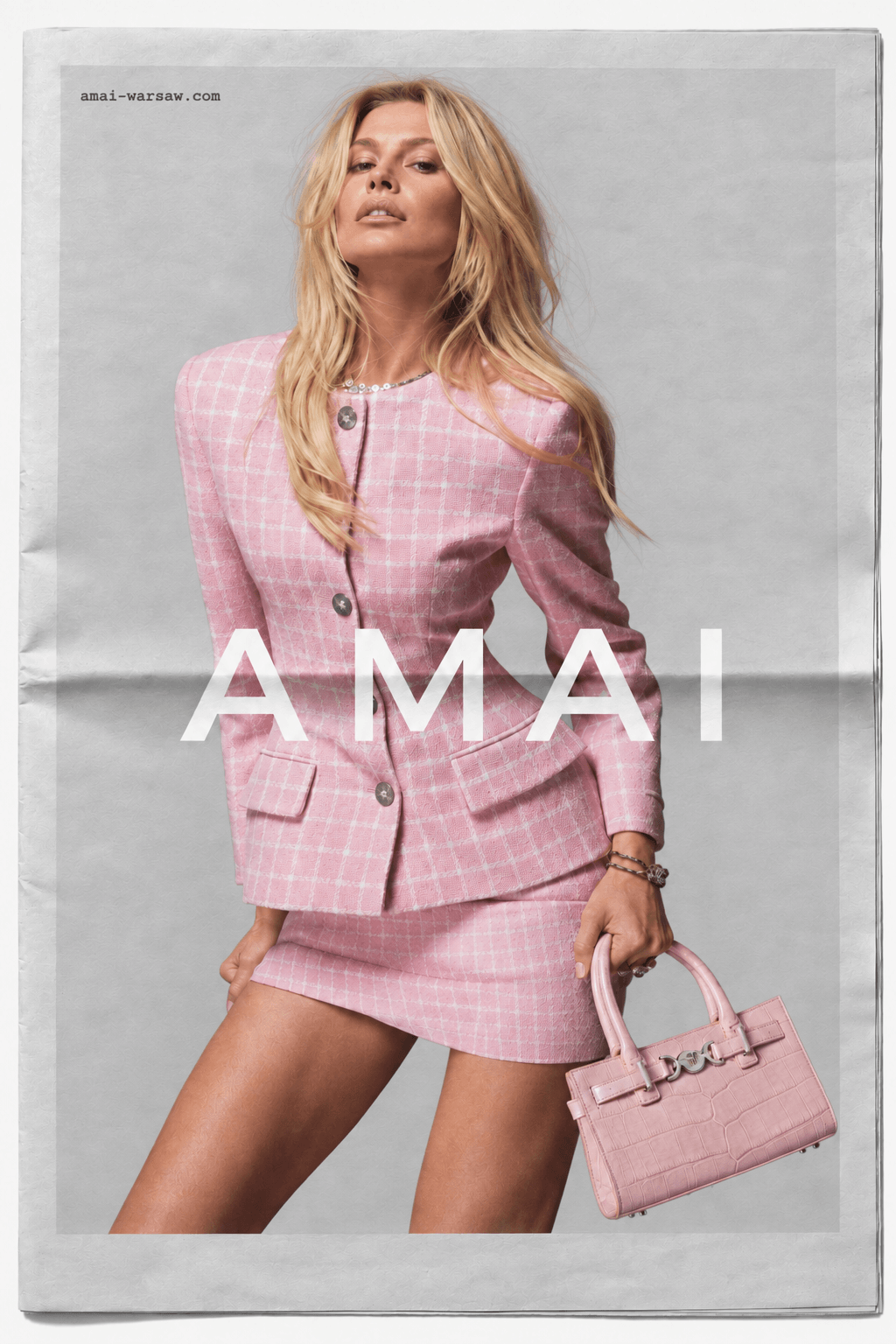 AMAI campaign printed as a folded newspaper page: a model in a pink tweed jacket and skirt holds a pink croc-embossed handbag, with the AMAI wordmark across the image.